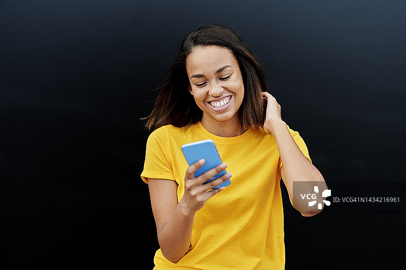 穿黄色T恤的女人在黑色背景上使用智能手机图片素材