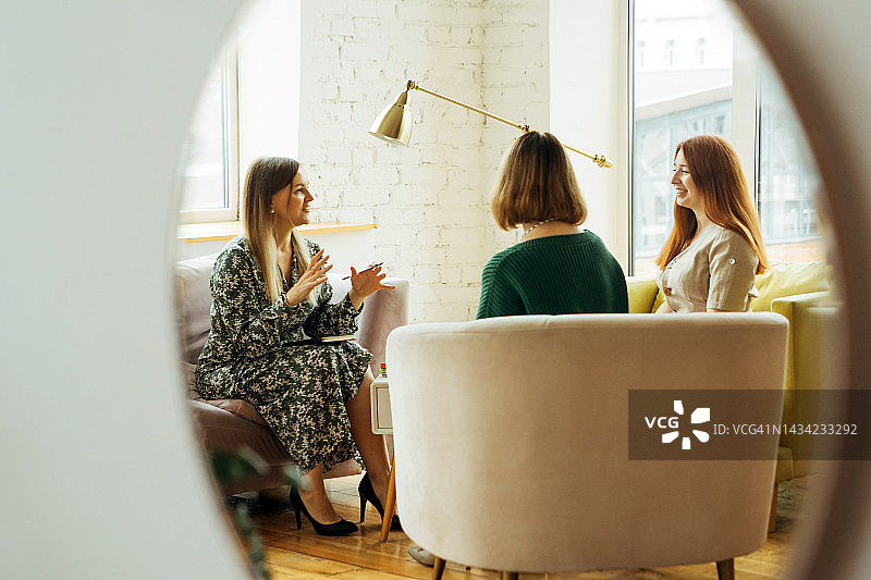 三位女性坐在扶手椅上交谈，镜中映出她们的身影图片素材