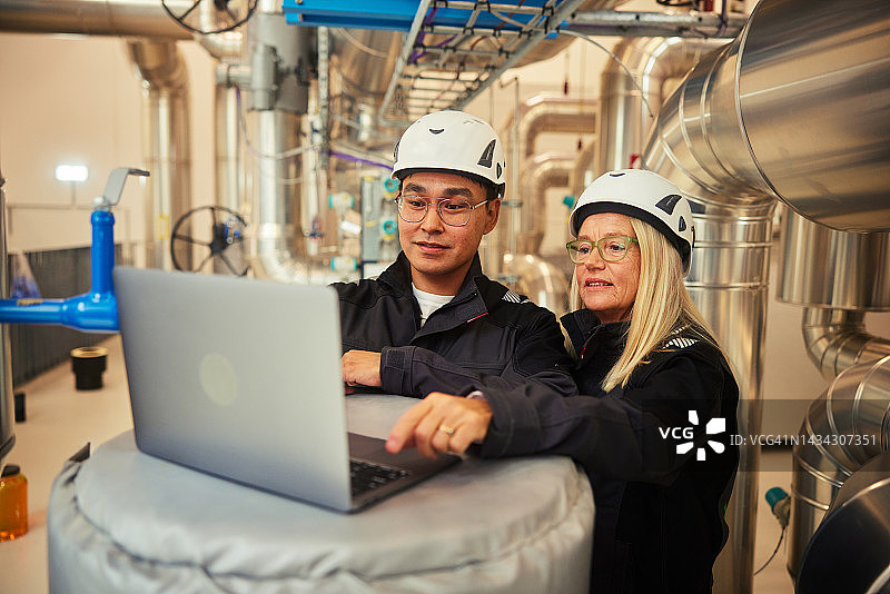 工程师在发电站的管道旁一起使用笔记本电脑图片素材