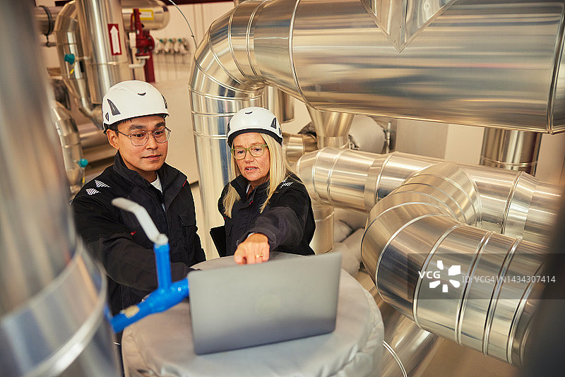 工程师在发电站管道旁一起使用笔记本电脑图片素材