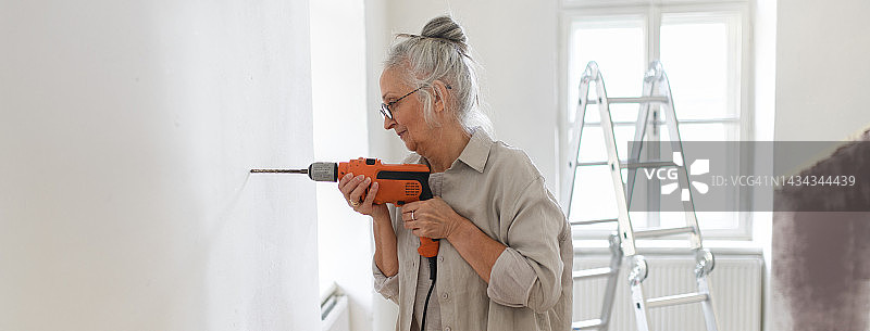 年长的女人在墙上钻孔，准备挂照片图片素材