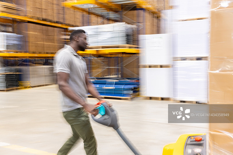 仓库员工用托盘车搬运货物箱的模糊景象图片素材