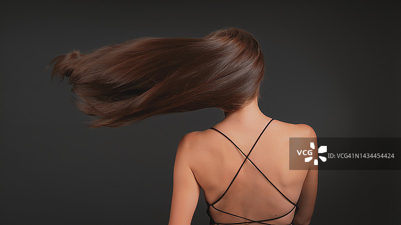 深色背景下迷人的棕发美女：闪亮健康的棕色头发随风飘动图片素材