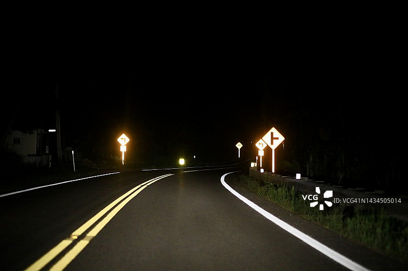 黑暗弯曲道路上的反光标志图片素材