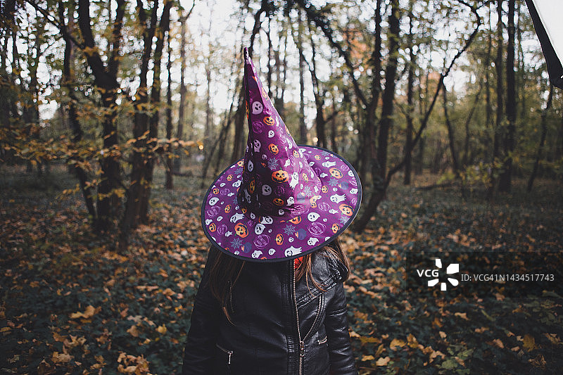 万圣节快乐！戴着女巫帽的女孩在树林里图片素材