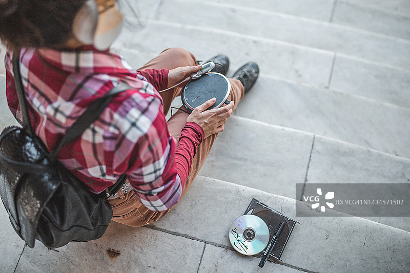 一位坐在楼梯上用迷你光盘播放器听音乐的女士（不可辨认）的俯视照片图片素材