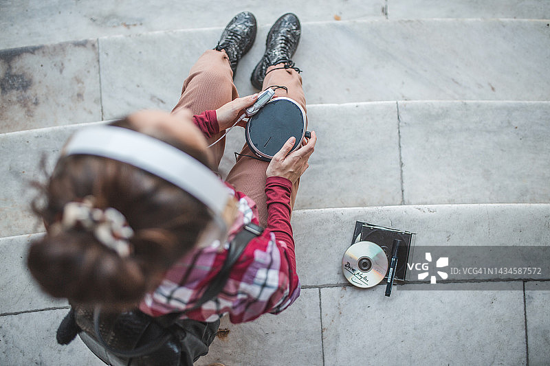 休闲装女子坐在楼梯上用迷你光盘播放器听音乐的顶视图图片素材