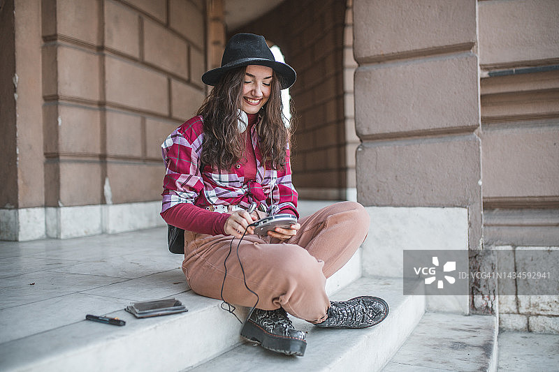 戴着帽子坐在楼梯上，用光盘播放器听音乐的微笑年轻女人图片素材