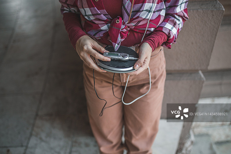 一名女子靠墙站着用CD机听音乐图片素材