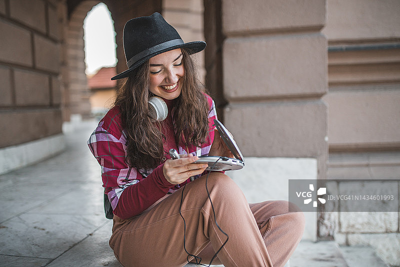 快乐的年轻女人在户外用迷你光盘播放器听音乐图片素材