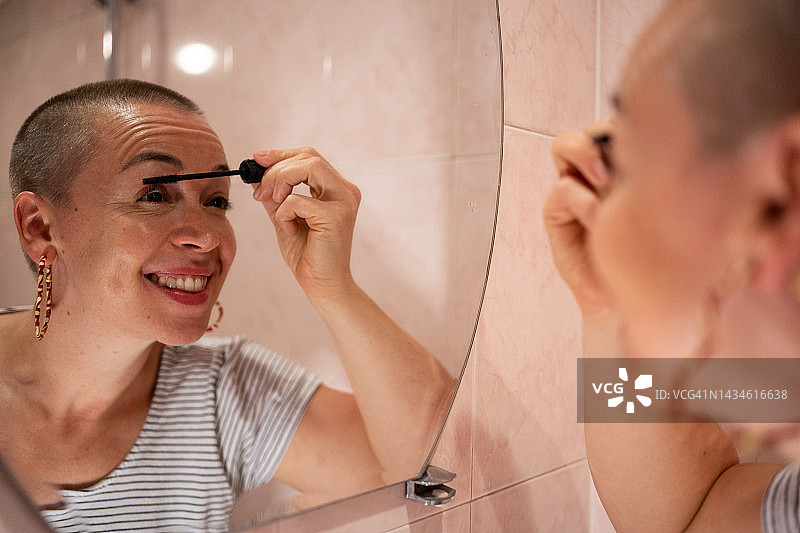 剃了头发的女人在镜子前涂睫毛膏图片素材