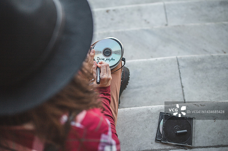年轻女人坐在台阶上，在光盘上写名字，光盘里是旅行音乐图片素材