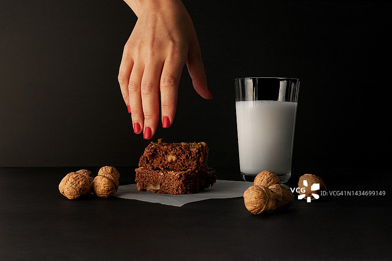 年轻女子的手在深色背景上拿着巧克力布朗尼图片素材