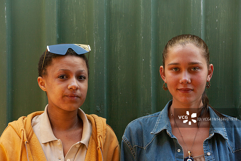 两位面带微笑的年轻女人并肩站在绿色背景前图片素材