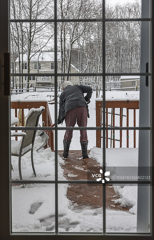 年长的女人在露台上用铲子清扫积雪图片素材