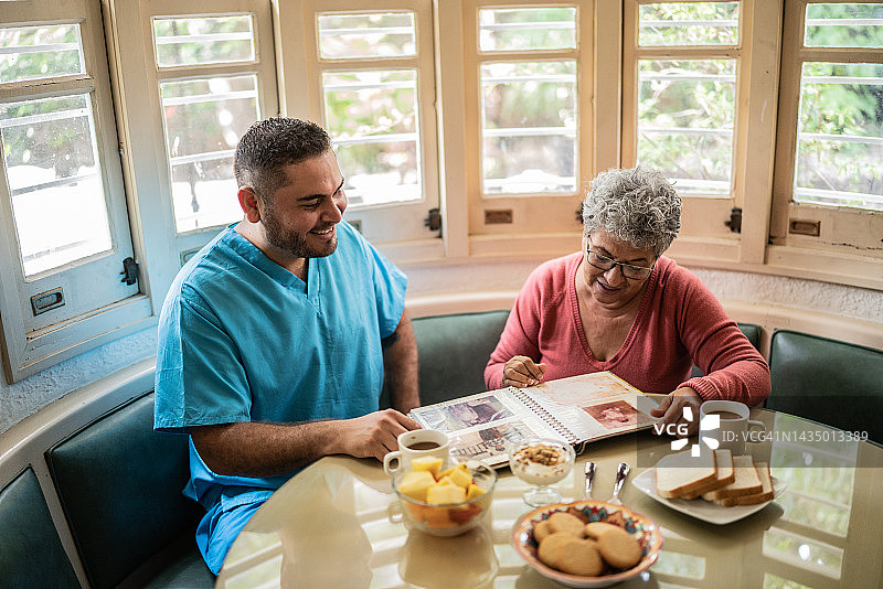 疗养院里，年长的女人和中年护士在餐厅里看相册图片素材