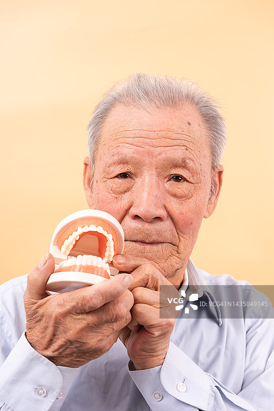 老人手持牙齿模型，牙齿健康与口腔护理概念图片素材