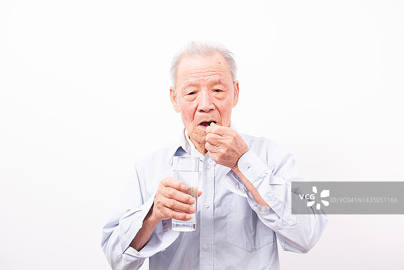 年长的男人拿着胶囊和一杯水，在白色背景下隔离图片素材