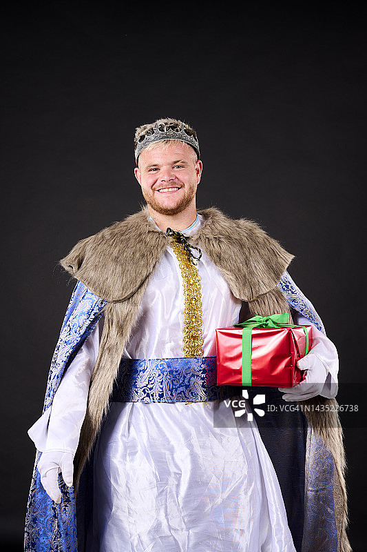 微笑的年轻男人戴着王冠和野牛披肩，拿着礼品盒看着镜头图片素材