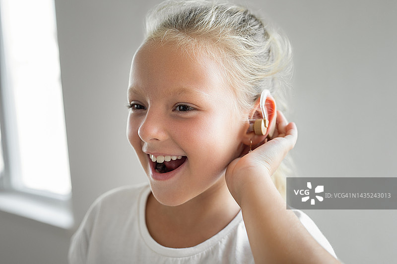 耳朵后面戴着助听器，面带微笑的女童图片素材