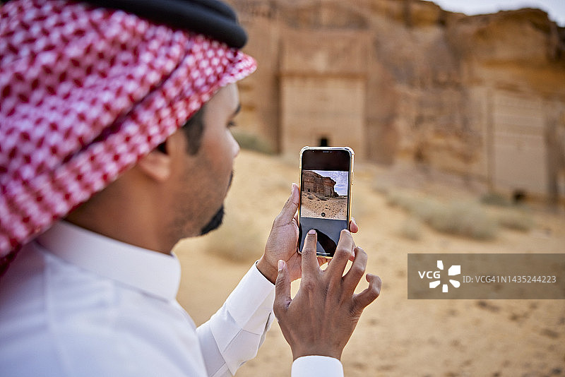 沙特阿拉伯男子用手机拍摄岩石墓葬，Hegra图片素材