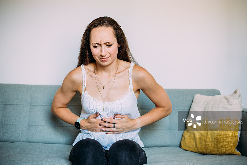 女人在家躺在沙发上时感到胃痛图片素材