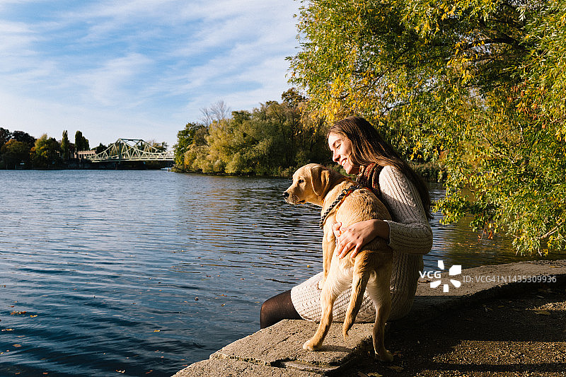 年轻女子坐在海滨，怀抱拉布拉多幼犬图片素材
