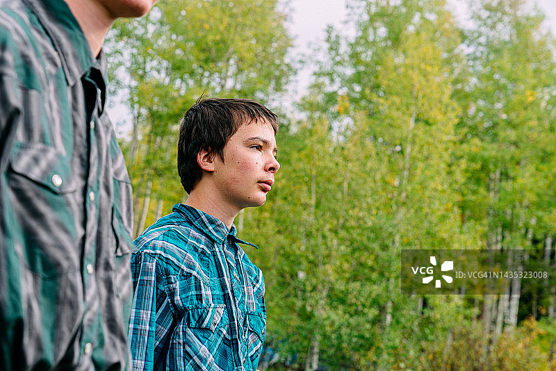 在美利坚科罗拉多州小镇家庭拥有的牧场上,一个坚忍的年轻少年牧场主与他的兄弟站在一起,目光离开相机,留有文案空间的低角度肖像图片素材