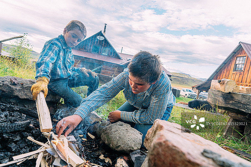 在美国科罗拉多州小镇家庭农场的后院里，年轻的白人牧场兄弟一起在火坑里生火图片素材