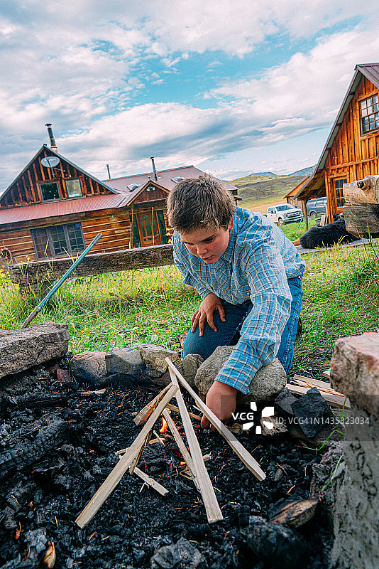 在美国家庭牧场后院的火坑旁生火的年轻白人男孩图片素材