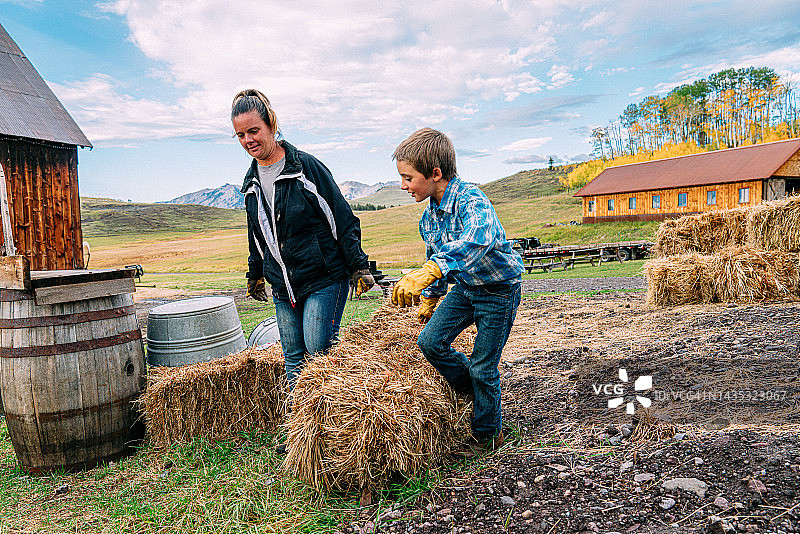 母亲和年幼的儿子在美国科罗拉多州的小镇家庭农场一起搬运干草图片素材