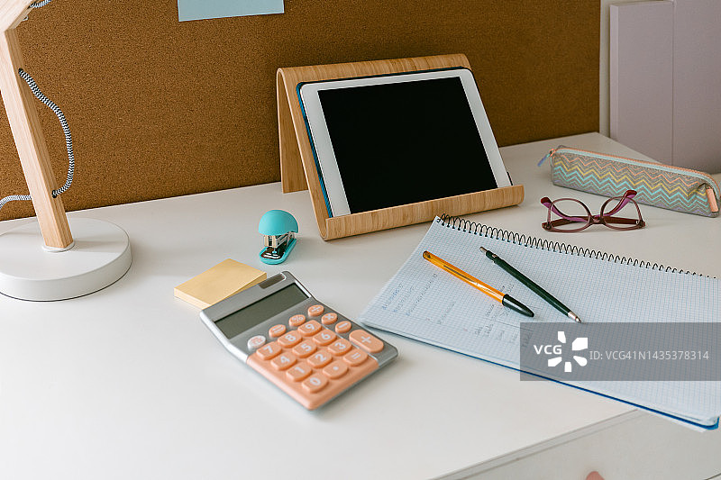 一个年轻女孩或青少年房间的白色书桌图片，下午学习，有计算器、平板电脑、铅笔盒和带有家庭作业的笔记本。工作区概念图片素材