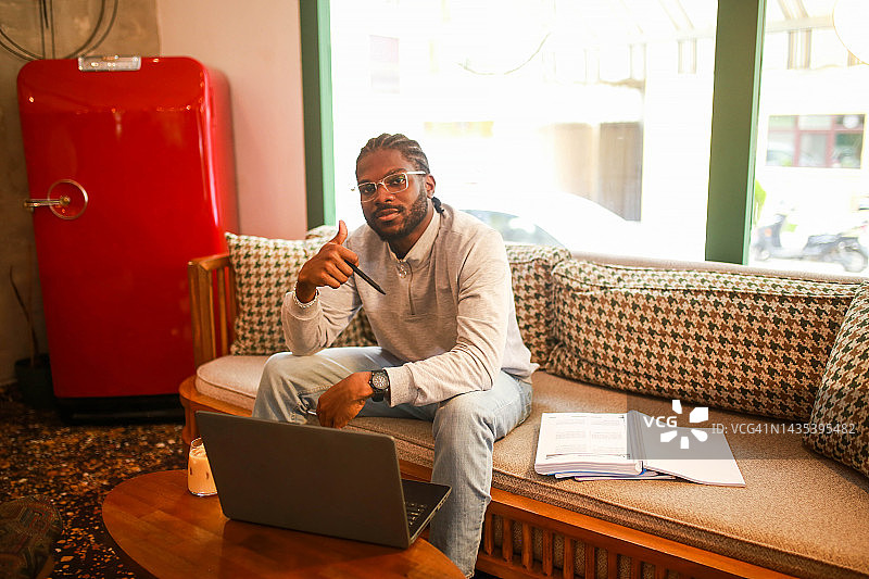 在咖啡馆用电脑学习并用手打勾的黑人男学生图片素材