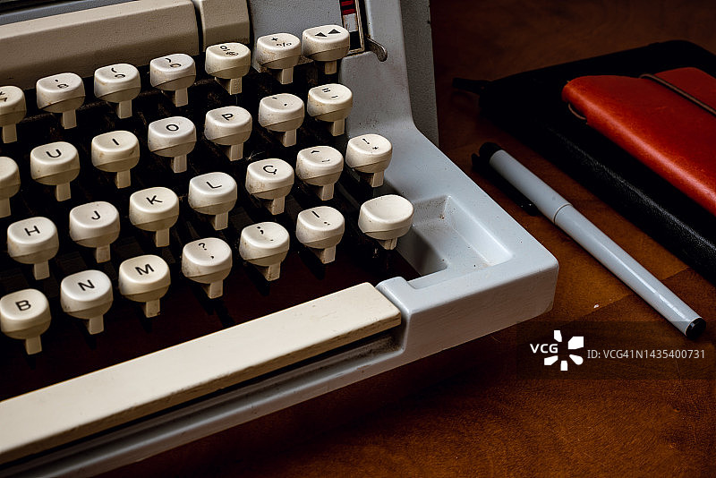 木制办公桌上的旧打字机和皮革笔记本特写图片素材