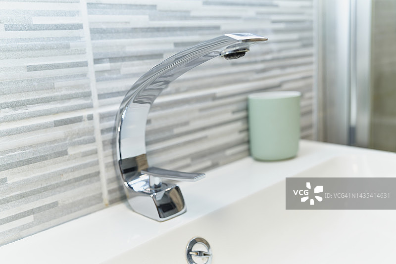 白色瓷洗手盆上的封闭式金属水龙头，彩色陶瓷墙图片素材