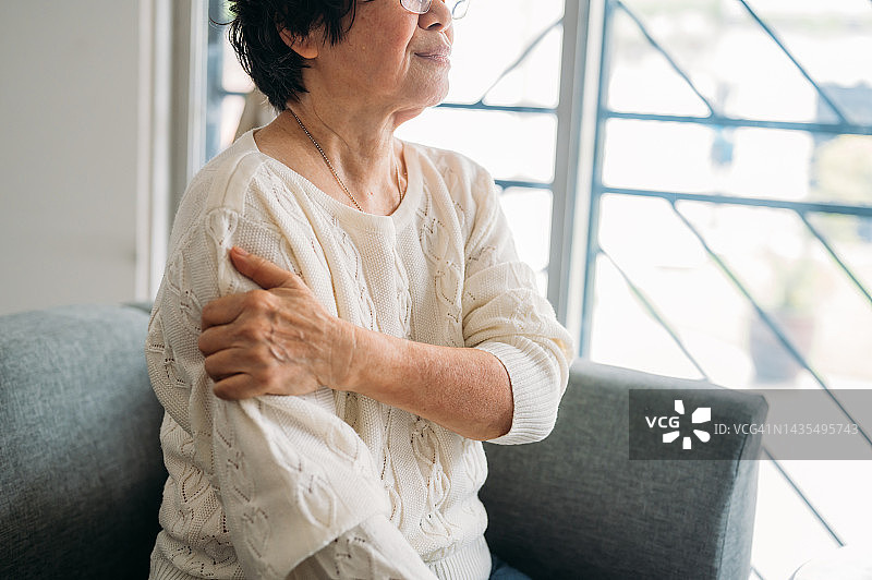 坐在沙发上感到肘部疼痛的年长的亚洲中国女人特写。在家中手部疼痛的老年妇女图片素材