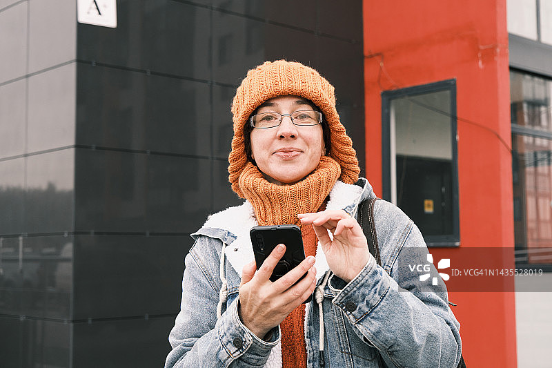 快乐的中年妇女穿着暖和的衣服在城市里使用手机图片素材