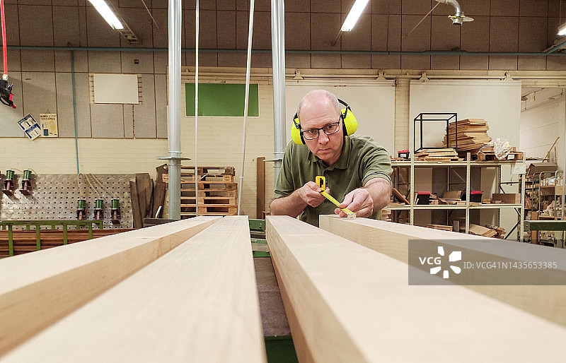一位白人男性木匠用建筑测量仪测量木条图片素材