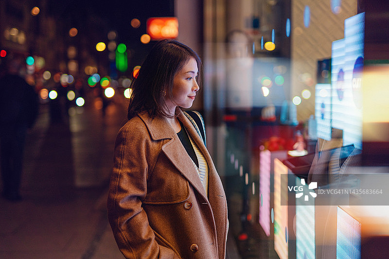 年轻女人在夜晚的城市街道上看商店橱窗图片素材