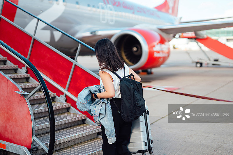 拉着行李箱，走在机场跑道上，走向飞机的年轻亚裔女性图片素材