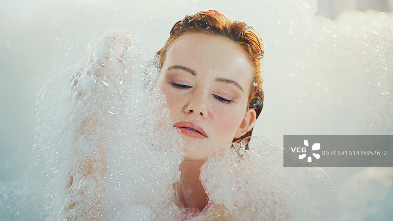 在浴缸里放松的红发蓝眼漂亮女人，进行自我护理和健康活动图片素材