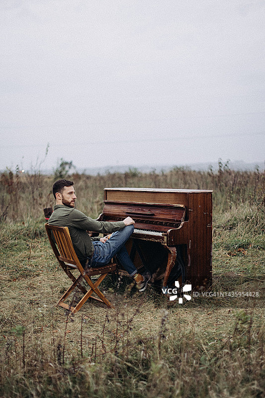 英俊男人坐在田野里的钢琴旁图片素材