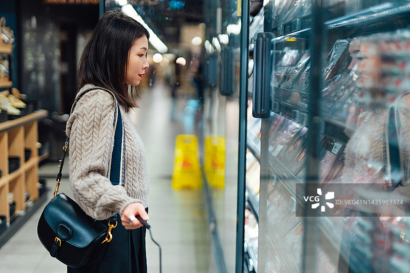 年轻的亚洲女性在超市的冰箱里挑选食物图片素材