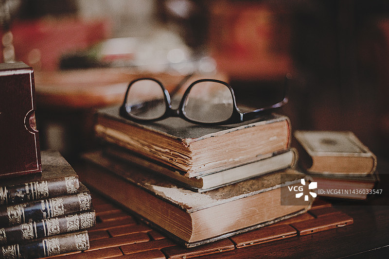 床头柜上堆叠旧书上的老花镜图片素材