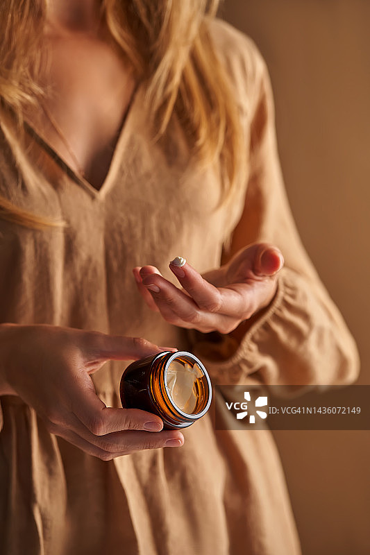 穿着米色连衣裙的女人手持天然化妆品面霜图片素材