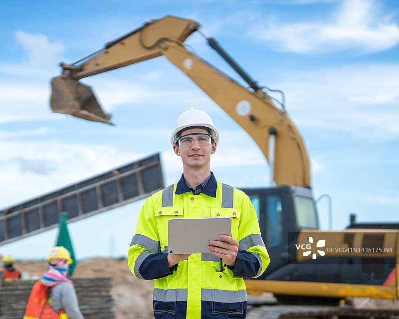 男工程师在建筑重型机械背景下使用平板电脑图片素材