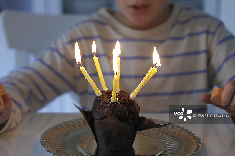 男孩吹灭生日纸杯蛋糕上的蜡烛图片素材