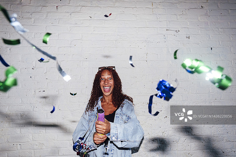 快乐的年轻女子在墙前玩派对礼炮图片素材