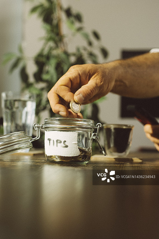 商人将硬币投入咖啡店的小费罐图片素材