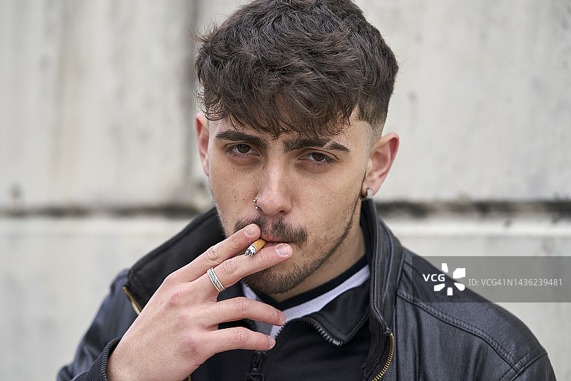 穿着黑色皮夹克在城市街道上吸烟的年轻男人图片素材